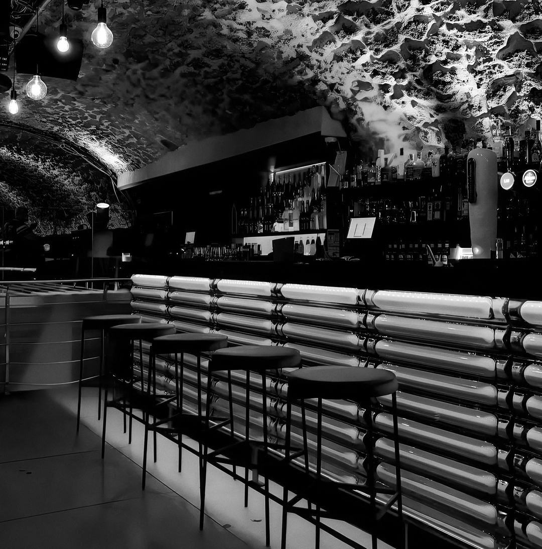 Le bar du Scotch sous la voûte de pierre : comptoir lumineux, tabourets hauts et ampoules à filament